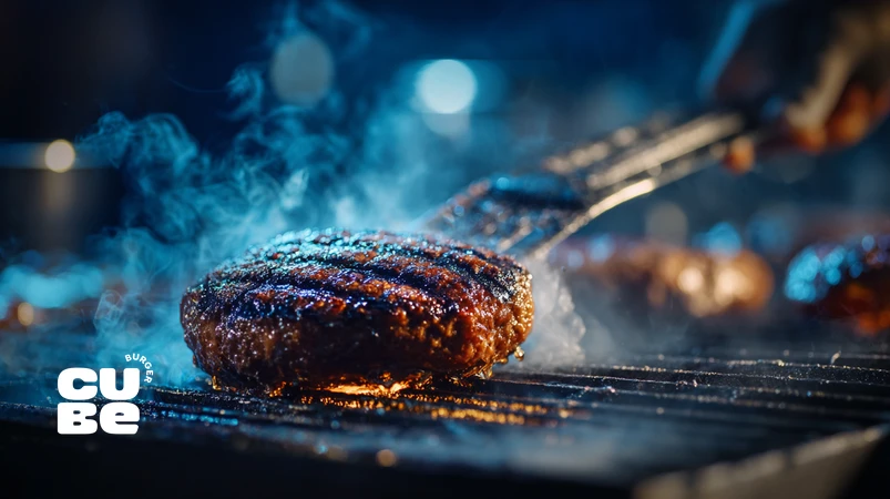 برگر زغالی آبدار روی گریل با پوسته کاراملی و دود آبی ملایم، در حال پخت حرفه‌ای با حرارت دو زون و طعم اصیل آتش‌کوره‌ای