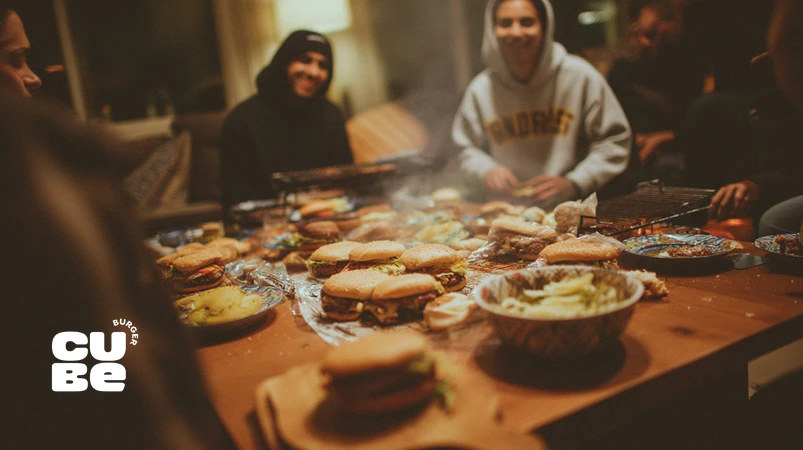 دورهمی دوستانه با برگر دست‌ساز روی میز چوبی، همراه با نان، سس‌ها و تاپینگ‌های متنوع برای راهنمای برگزاری برگرپارتی